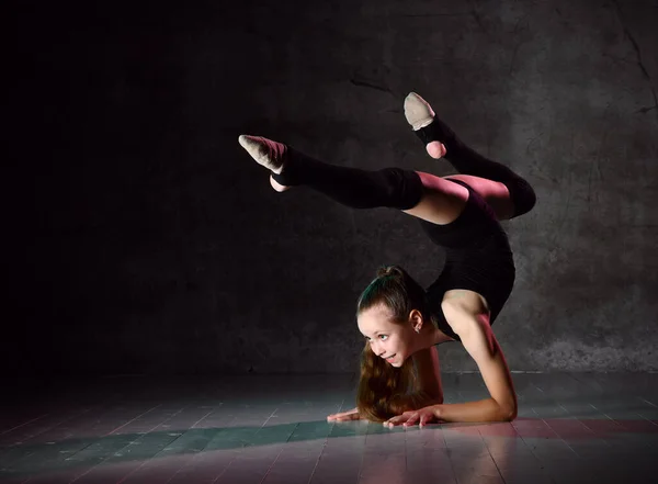 Подростковая гимнастка в черном трико, носки на коленях и балетные туфли, выполняющая упражнения стоя на руках, вверх ногами. Крупный план — стоковое фото