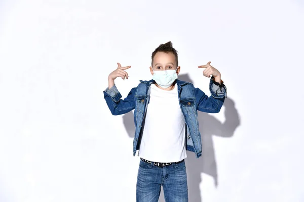 Ragazzo biondo con jeans blu, giacca, t-shirt. E 'in maschera medica, sembra confuso, posa isolato sul bianco. Coronavirus — Foto Stock