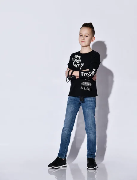 Adolescente en jersey negro y zapatillas de deporte, vaqueros azules, pulsera. Se puso de pie con las manos cruzadas, posando aislado sobre fondo blanco — Foto de Stock