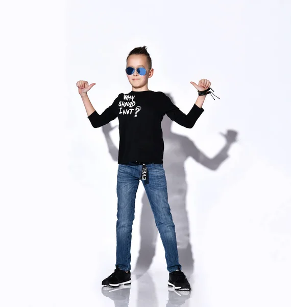Adolescente do sexo masculino em óculos de sol, jumper preto e tênis, jeans, pulseira. Ele sorrindo, mostrando os polegares para cima, posando isolado no branco — Fotografia de Stock