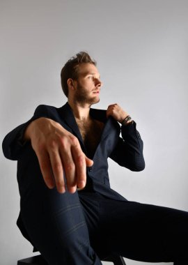 Mavi takım elbiseli seksi adam çıplak vücutta. Ceketini düzeltiyor, siyah merdivende oturuyor, beyaz üzerine izole poz veriyor. Kapat.