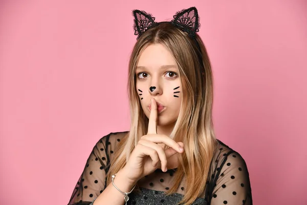Ungdom i svart klänning, pannband som kattöron, ansiktsmålning. Hon visar vara tyst tecken, poserar på rosa bakgrund. Närbild — Stockfoto