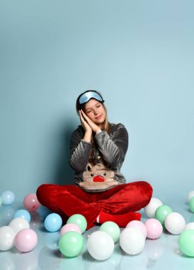 Ren geyiği pijamalı genç kız, kırmızı çoraplar, uyku maskesi. Gözleri kapalı, yerde oturuyor, balonlar, mavi arka plan. Kapat.