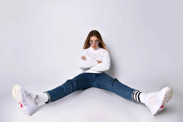 Adolescente em óculos de sol, jeans, suéter, meias e tênis. Posando sentado no chão, pernas afastadas, isoladas em branco. Fechar — Fotografia de Stock