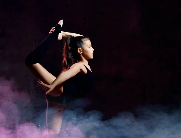Mała dziewczynka w czarnej gimnastyce gimnastyczka wykonuje ćwiczenia. Równowaga na jednej nodze z uchwytem. — Zdjęcie stockowe