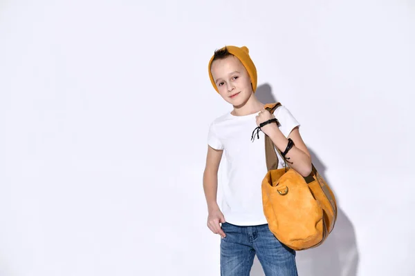 ポートレートオレンジ色の旅行バッグを持つ10代の子供は、帽子、サングラス、 Tシャツ、ブルーデニムスーツ、ブラックスニーカー、ブレスレットを身に着けています。. — ストック写真