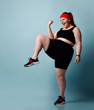 Gülümseyen büyük beden kız egzersizleri yapıyor yerine geçiyor mavi arka planda dizlerini kaldırıyor. Fitness Tam boy portre, kopyalama alanı