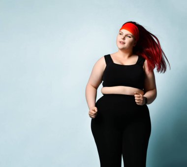 Sakin, düşünceli, genç ve iri yarı bir model mavi arka planda rüya gibi bir gülümsemeyle yavaş yavaş koşuyor. Fitness, motivasyon, vücut pozitifliği. Boşluğu kopyala