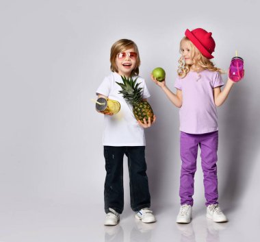 Çocuklar, renkli günlük kıyafetler. Gülen, elinde sarı ve pembe kokteyl şişeleri tutan, elma, ananas. Beyaz üzerine izole edilmiş pozlar