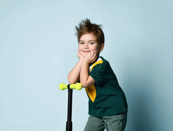 Renkli tişörtlü çocuk. Mavi arka planda tekme scooter 'ı üzerinde dururken gülümsüyor. — Stok fotoğraf