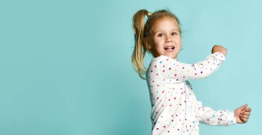 Kalp şeklinde bir tişört giymiş sarışın bir çocuğun portresi. Gülümsüyor, takılıyor, naneli bir stüdyonun arka planında eğleniyor.