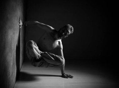 Kahverengi pantolonlu çıplak bir adam yoga yapıyor. Nilüfer çiçeğinin bacakları, bir elini duvara, diğerini de yere koyar.