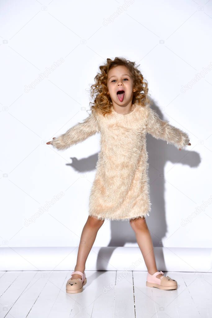 Joyful curly blond girl in pink flossy dress and sandals joking spreading arms and legs widely and lolling out. Full length portrait isolated on white