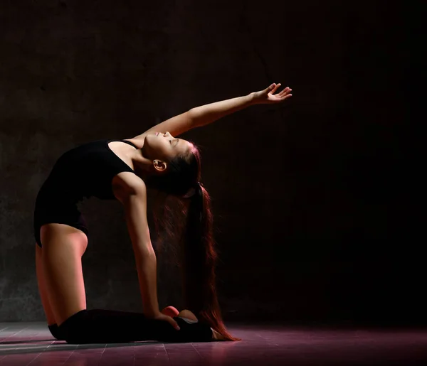 Giovane ginnasta ragazza in corpo nero sport e calzature speciali fare posa ginnastica su sfondo scuro — Foto Stock
