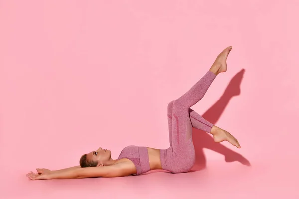 사랑 스러운 아가씨가 누워서 손을 뻗고 다리를 힘있게 하는 운동을 하고 있습니다. 분홍, 복사 공간에 고립된 스튜디오 사진 — 스톡 사진