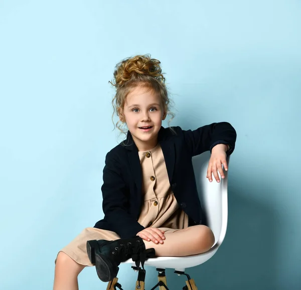 Adorabile ragazza bionda con elegante acconciatura alta seduta rilassatamente su una sedia da ufficio che mostra un sorriso dolce. Studio girato isolato su blu — Foto Stock