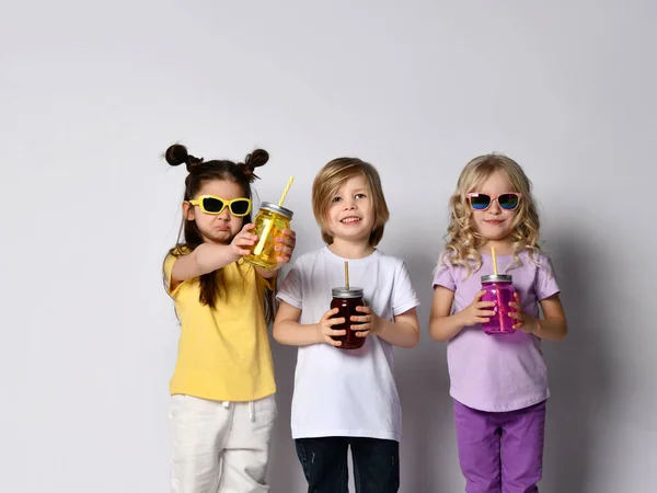 Маленький хлопчик і дівчатка в сонцезахисних окулярах, барвистий повсякденний одяг. Вони тримають пляшки коктейлю і посміхаються, позує ізольовано на білому — стокове фото