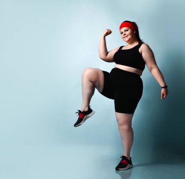 Aktif gülümseyen büyük beden kız egzersizleri yapıyor, yerine geçip dizlerini yukarı kaldırıyor, mavi arka planda. Fitness Tam boy portre, kopyalama alanı