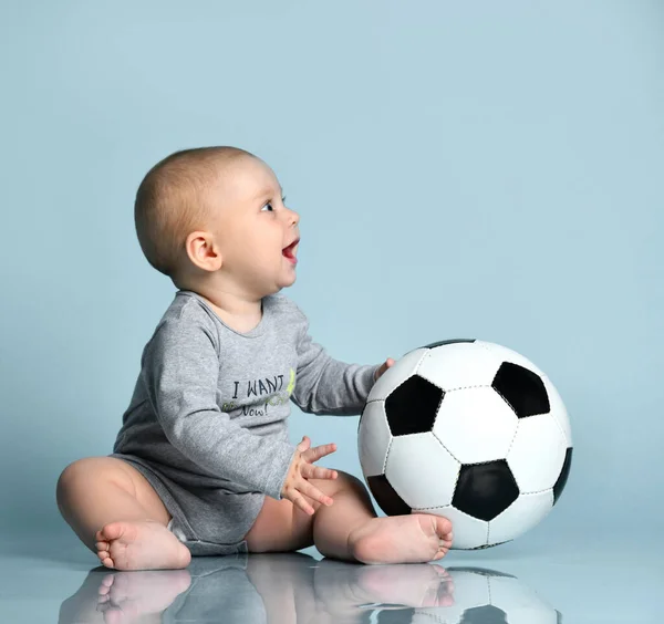 Niño jengibre en traje gris, descalzo. Sostenía la pelota de fútbol, sentado en el suelo sobre fondo azul. Cerrar, copiar espacio —  Fotos de Stock