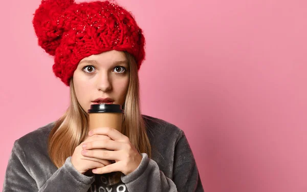 Ragazza in pigiama grigio, cappello rosso. Lei è in possesso di un bicchiere di carta e andare a bere, in posa su sfondo rosa. Da vicino. — Foto Stock