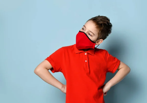 Adolescent en t-shirt rouge et masque de protection. Il posa les mains sur les hanches, posant sur fond bleu. Concept de coronavirus — Photo
