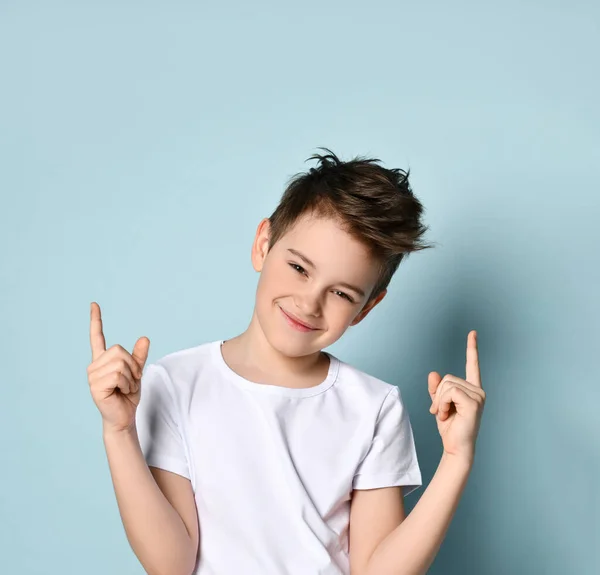 Un adolescente con una camiseta blanca. Sonrió, levantó a sus antepasados, posando sobre fondo azul del estudio —  Fotos de Stock