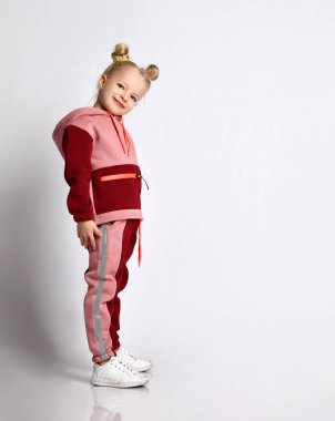 Renkli eşofmanlı, spor ayakkabılı, küçük sarışın manken. Gülümseyen, egzersiz yapan, beyazlar üzerinde yalnız poz veren