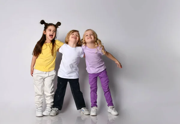 Маленький хлопчик і дівчатка одягнені в різнокольоровий повсякденний одяг. Вони посміхаються і обіймаються один з одним, позує ізольовано на білому — стокове фото
