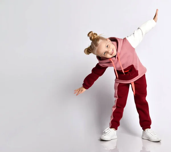 Kleine blonde jongen met een kontje kapsel, in kleurrijke trainingspak, sneakers. Lachen, oefeningen doen, geïsoleerd poseren op wit — Stockfoto