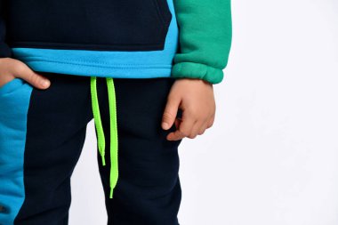 Little male in colorful tracksuit. He has put one hand in pocket, posing isolated on white studio background. Fashion, advertising clipart