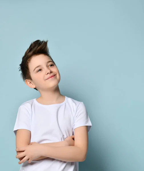 Adolescente con corte de pelo elegante, vestido con camiseta blanca. Sonriendo, dobló las manos y mirando hacia arriba, posando sobre fondo azul —  Fotos de Stock