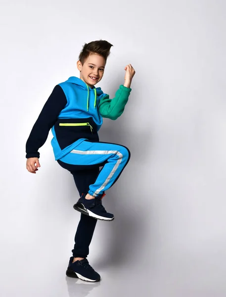 Pequeño modelo morena en traje deportivo colorido, zapatillas negras. Realizando ejercicios, sonriendo, posando de lado aislado sobre blanco Fotos de stock libres de derechos