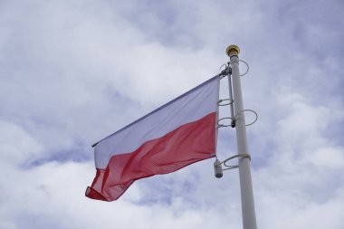 Yakın plan, bulutlu bir günde rüzgarda dalgalanan Polonya beyaz ve kırmızı bayrağı. Polonya bayrağının çekildiği gün,.