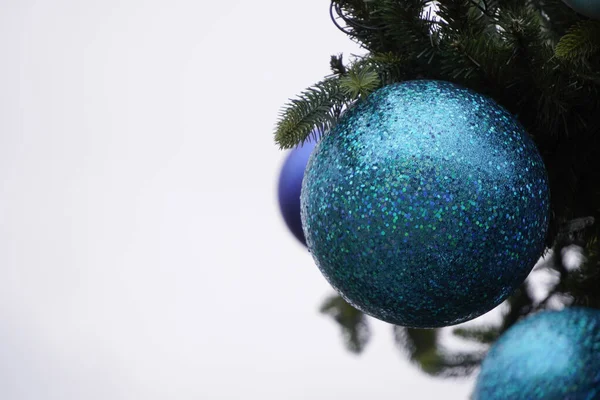 Jasnoniebieska błyszcząca piłka wisząca na choince na białym niebie, zachmurzona. spotkanie noworoczne lub Boże Narodzenie. — Zdjęcie stockowe