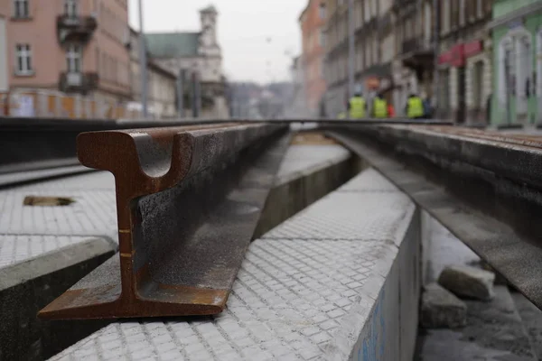 Construcción de vías para tranvías en el casco antiguo. los carriles oxidados de cerca, los trabajadores de la ciudad y la construcción en chalecos amarillos están borrosos en el fondo. reparación de carreteras — Foto de Stock