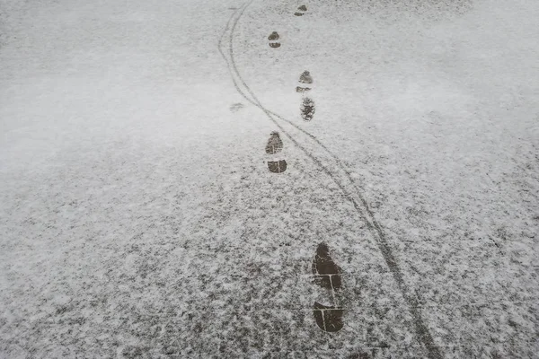 Man fotspår och hjul på den nyfallna snön på asfalten. vinterns första steg, årstidernas växlingar i början av vintern. Global uppvärmning — Stockfoto
