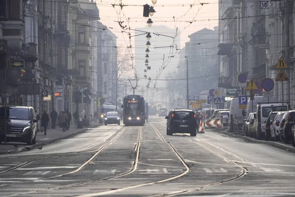 Cracovia, Polonia, 12.17.2019: el tranvía circula en una ciudad europea brumosa, luces que cuelgan sobre la carretera. red de transporte público de ciudad. La gente en la niebla va a trabajar, las luces del tranvía están encendidas . — Foto de Stock