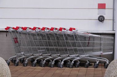 Süpermarketlerdeki veya mağazalardaki ürünler için demir arabaları. Kırmızı saplı market arabalarını park et. Satın alma sırasında ağır ürünlerin taşınması. Market arabaları üst üste yığılmış.