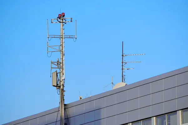 Uma antena com múltiplos transmissores e receptores montados no telhado de um prédio de escritórios possui faróis vermelhos intermitentes. A antena está perto do aeroporto — Fotografia de Stock