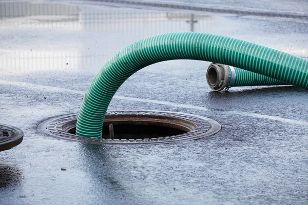 the green thick hose from a sewer pit, pumping sewage or sewage from collector in city. water drainage. Sewer manhole with an open manhole cover and large corrugated suction hoses for waste disposal