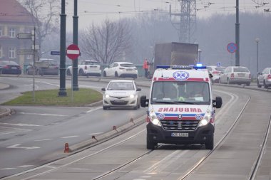 Cracow, Polonya 12.17.2019: acil durum ambulansı, tramvay raylarındaki bir hastaya yardım etmek için yanıp sönen ışıklarla hızla ilerliyor. Yol servisine fenerler açık, trafik güvenliği var.
