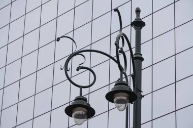 Eski tarz şehir feneriyle bir ofis binasının mavi modern cam cephesine karşı, şehirde sokak lambası. Eski ve yeni bir kombinasyon.