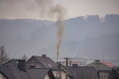 Kara duman gri gökyüzüne karşı bir evin bacasından gelir, kışın kömürle ısınır. Beskid Dağları, Zywiec, Krakow 'daki çevresel sis sorunu. Isıtma sisteminin güncellenmesi gerekiyor.