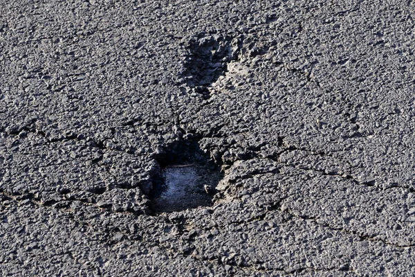 Pits, holes in the asphalt, poor asphalt road surface. Quality of asphalt laying. The problem of bad roads, road construction, poor quality asphalt