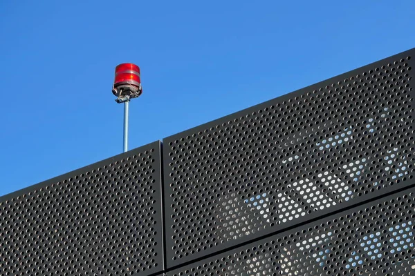 Sinal vermelho no telhado de um edifício perto do aeroporto. A estrutura metálica da fachada é preta contra o céu azul. Segurança das aeronaves — Fotografia de Stock