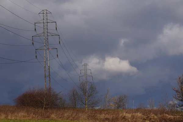 Power lines in the field against the background of a bright sky with dark snow clouds and highlighted by contrasting light from the sun. high voltage power lines go into the distance