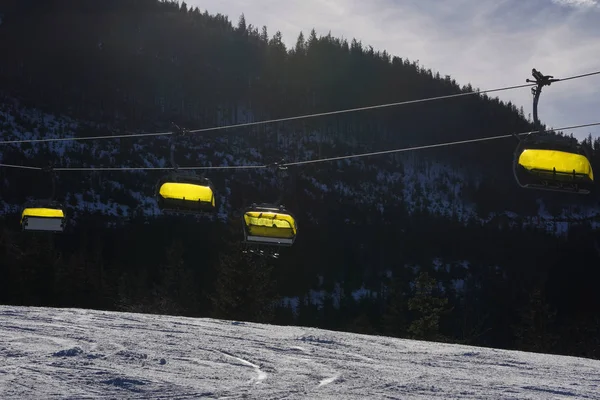 Ropeway cadeira vazia nas montanhas com uma cabine de cobertura amarela ou tampado. Elevador de cadeiras subindo a montanha. Szczyrk, Silésia . — Fotografia de Stock