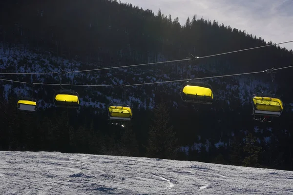Ropeway cadeira vazia nas montanhas com uma cabine de cobertura amarela — Fotografia de Stock
