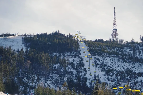 Cableway ou cadeira elevador com capas amarelas em uma estância de esqui no fundo de uma montanha e um transmissor de sinal em um dia nublado de inverno . — Fotografia de Stock