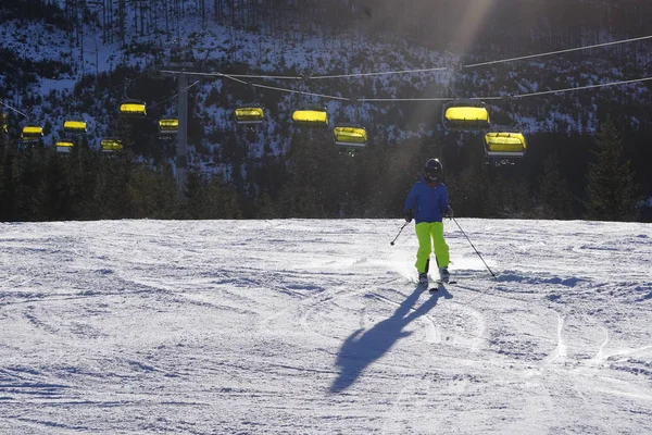 Uma pessoa em roupas brilhantes desce em esquis em uma estância de esqui. Recreação de inverno, esportes ou tempo de treinamento. A pessoa desce a montanha — Fotografia de Stock